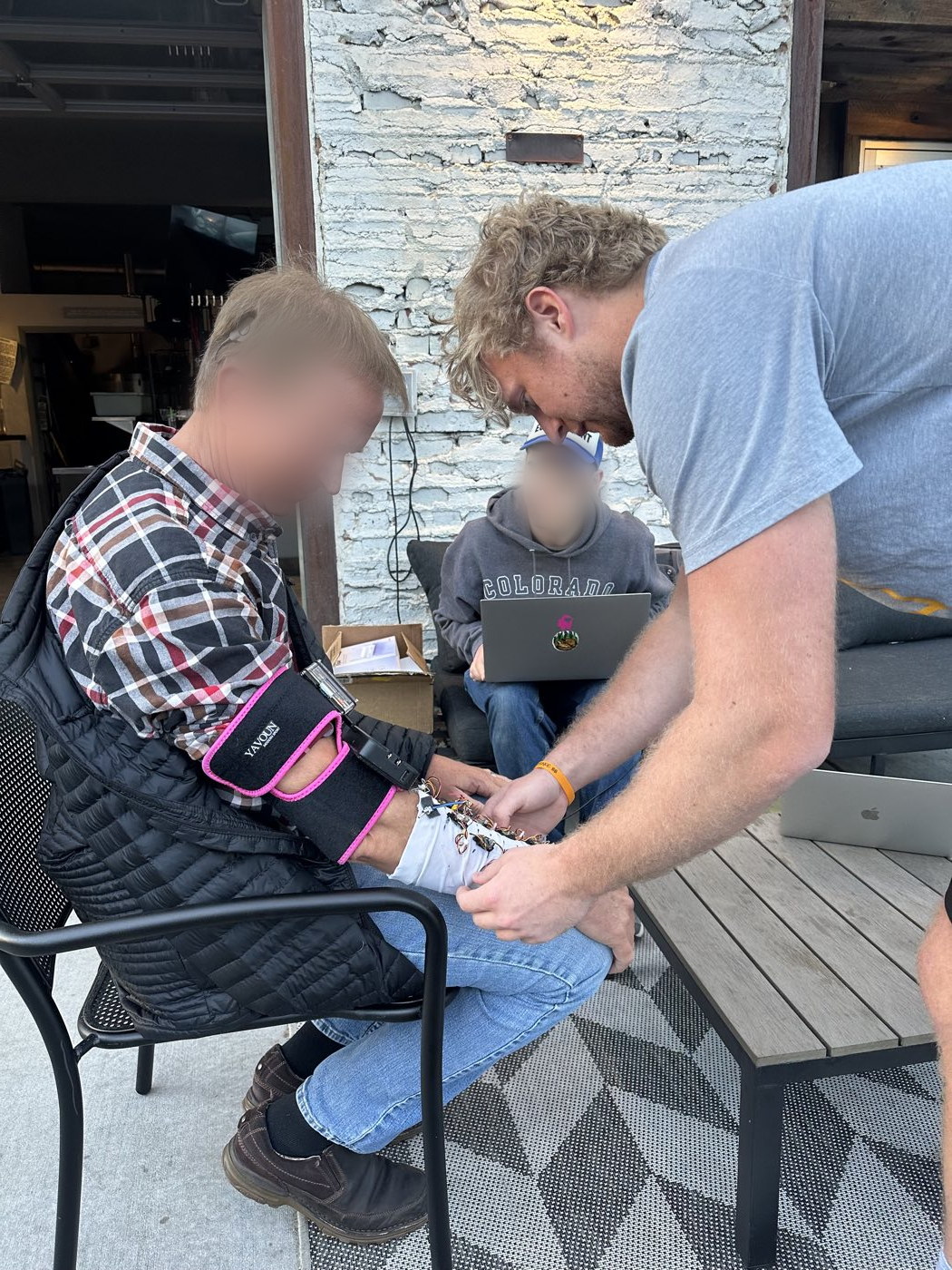 A team member fitting the early forearm rig onto a user seated in a patio chair